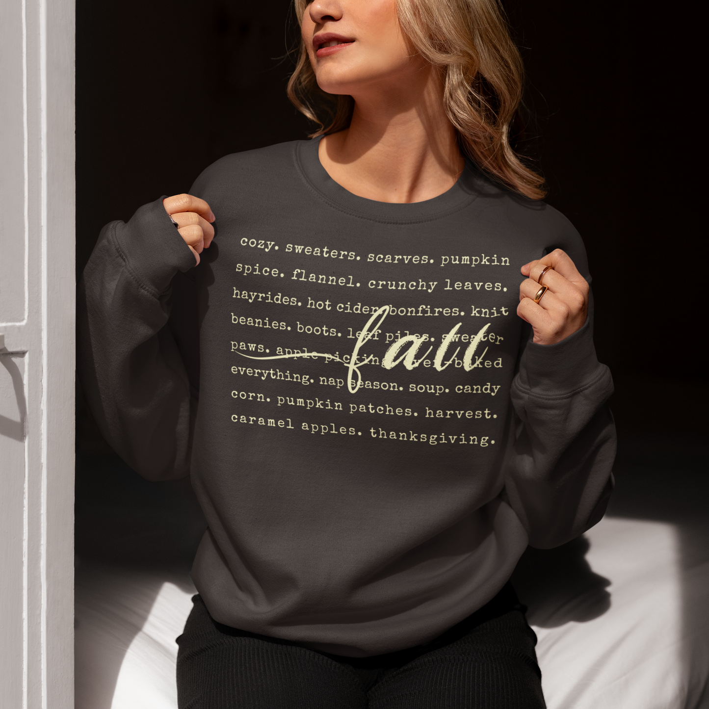 Person wearing a black sweatshirt with 'fall' and related词语 printed on it, sitting against a dark background.