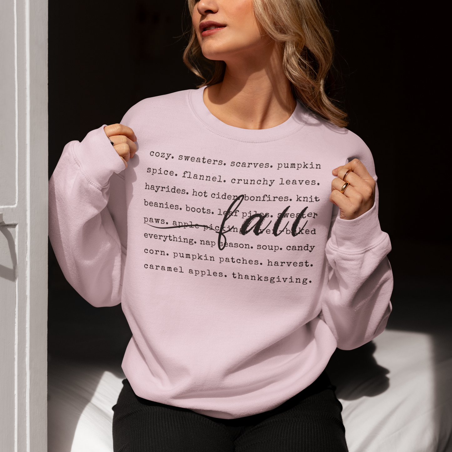 Person wearing a pink sweatshirt with text on it, sitting against a dark background.