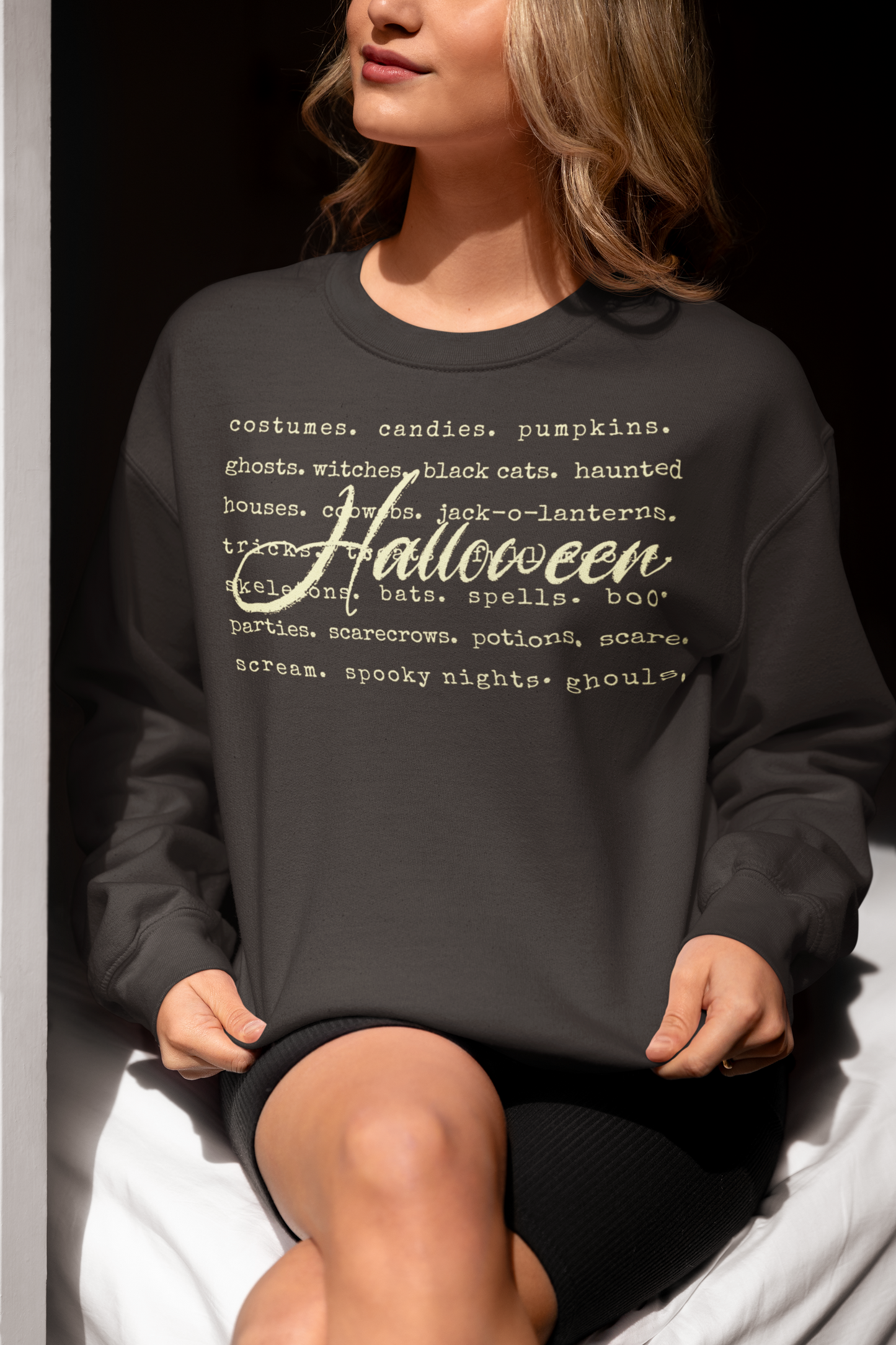 Person wearing a black sweatshirt with Halloween-themed text sitting against a dark background