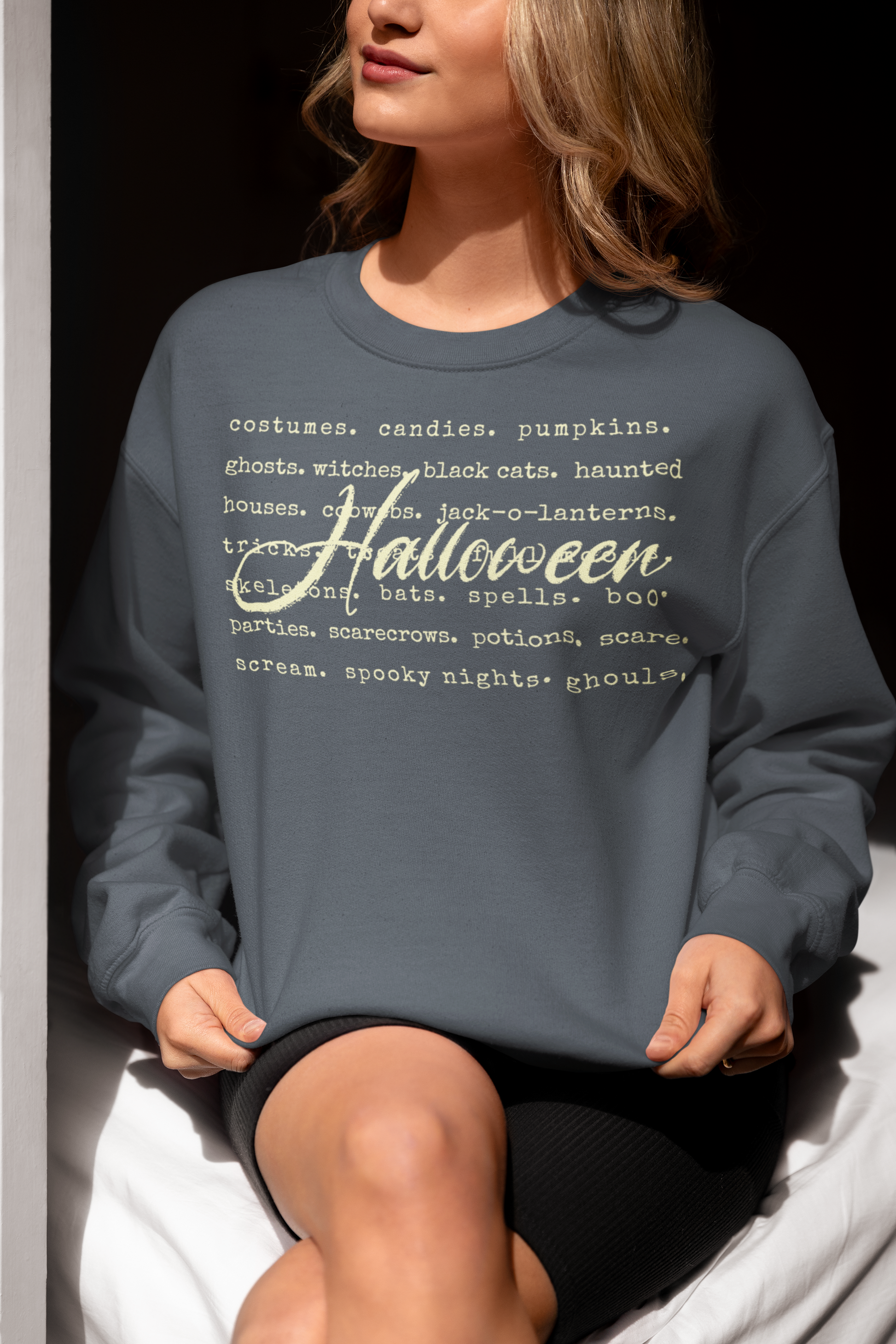 Person wearing a blue sweatshirt with Halloween-themed text sitting on a white surface.