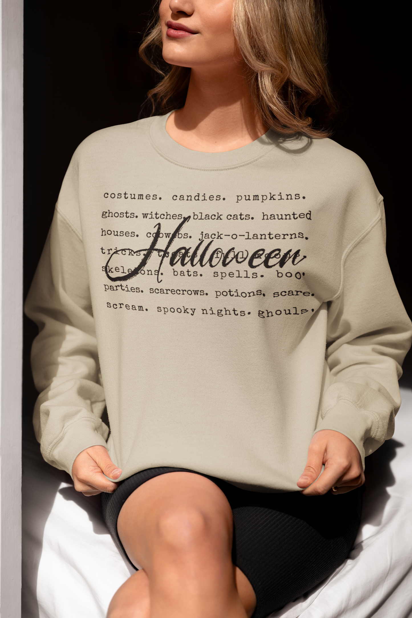 Person wearing a light gray sweatshirt with Halloween-themed text sitting on a white surface.