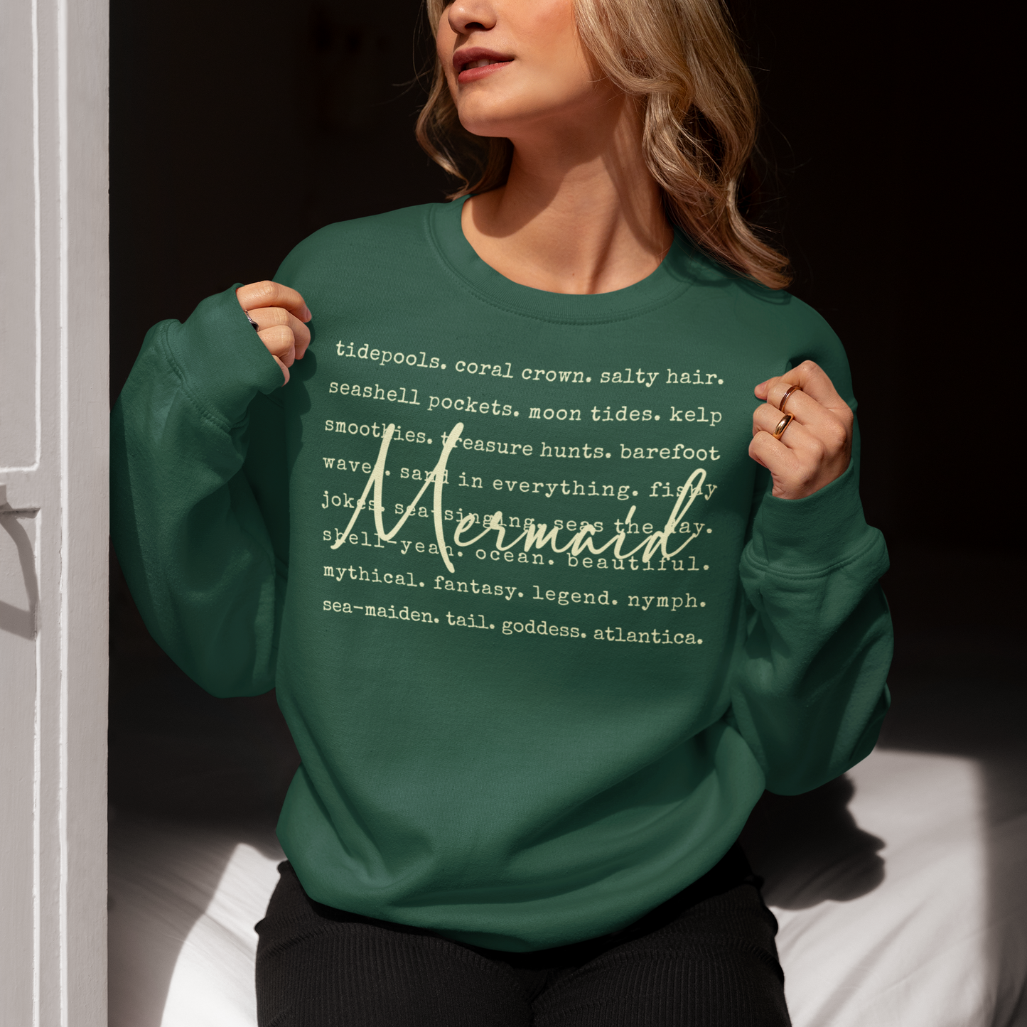 Person wearing a green sweatshirt with text design, sitting on a white surface.