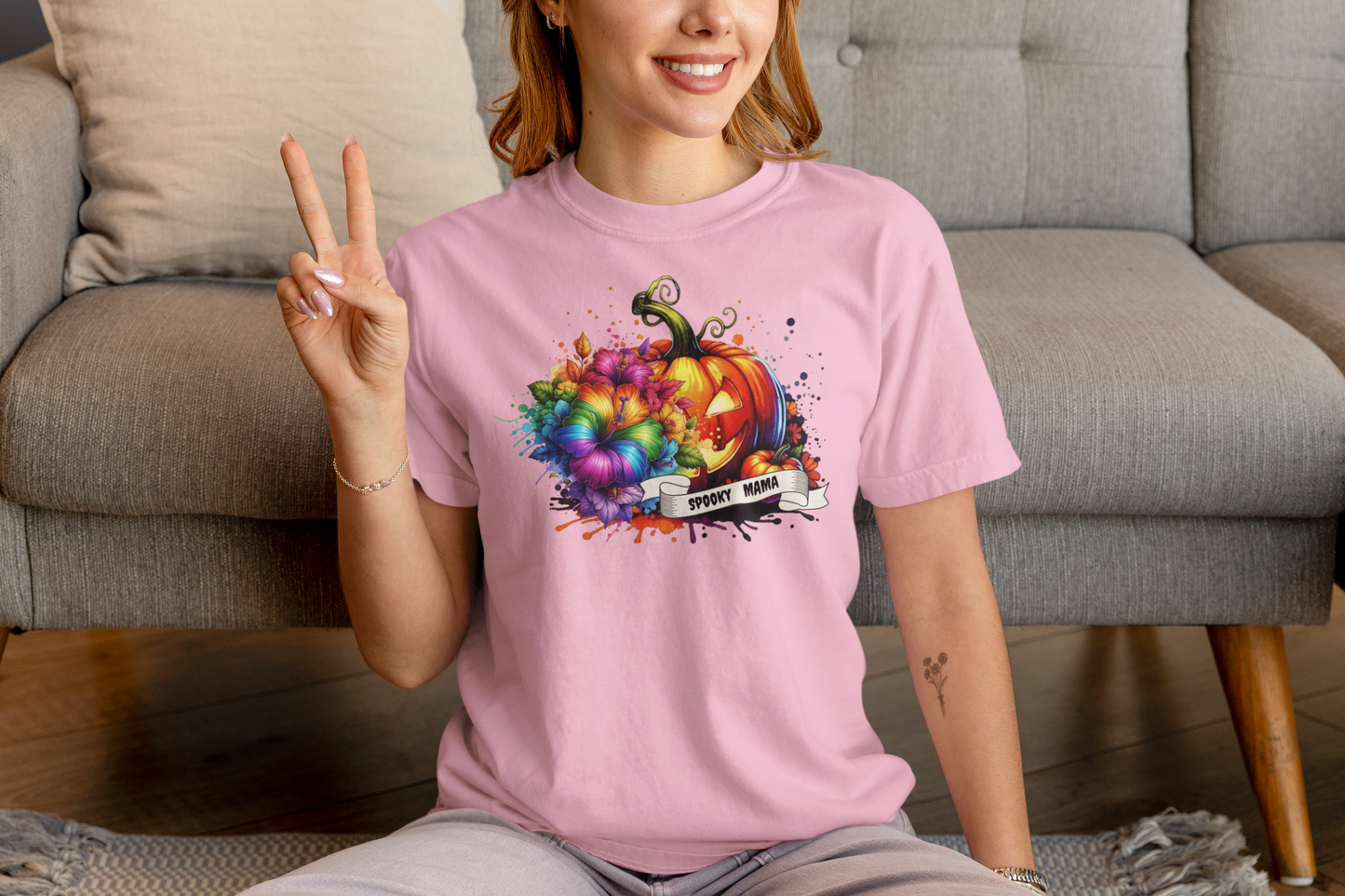 Person wearing a pink t-shirt with a colorful pumpkin design, sitting on a couch.
