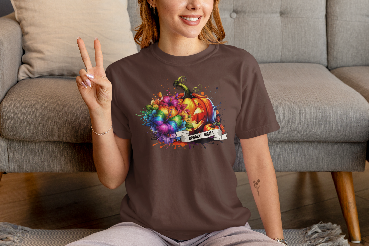 Person wearing a brown t-shirt with a colorful pumpkin design, sitting on a couch.