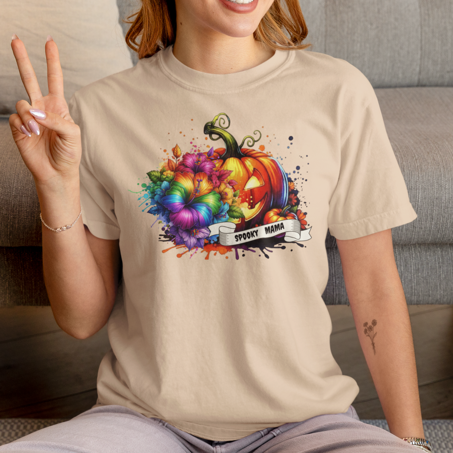 Person wearing a beige t-shirt with a colorful pumpkin design and 'Spooky Mama' text.