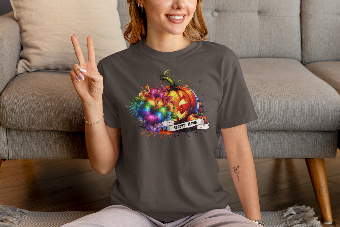 Person wearing a dark gray t-shirt with a colorful pumpkin design, sitting on a couch.