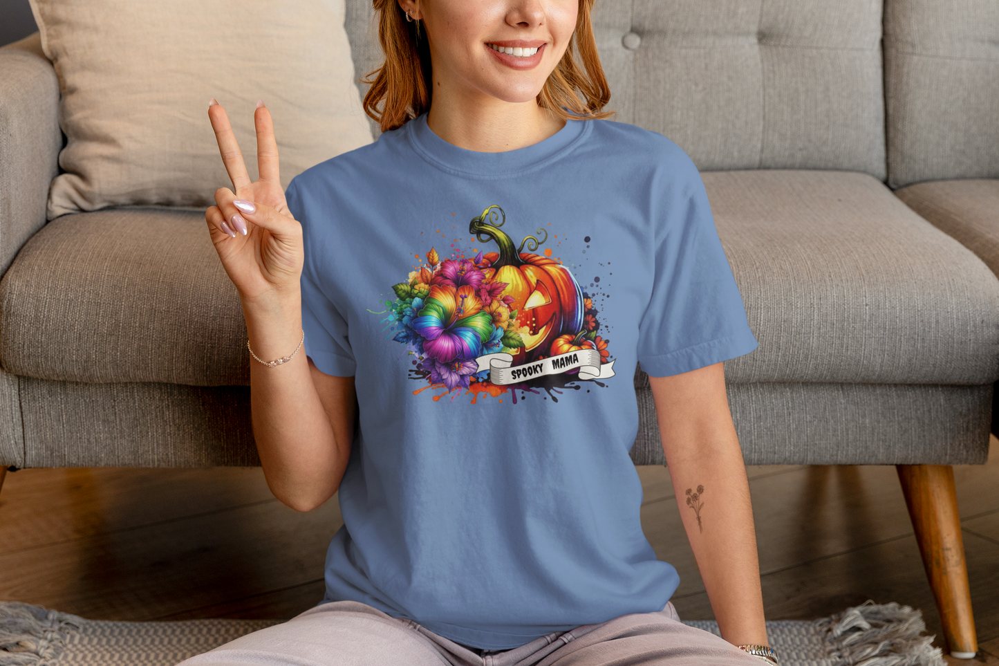Person wearing a blue t-shirt with a colorful pumpkin design, sitting on a couch.
